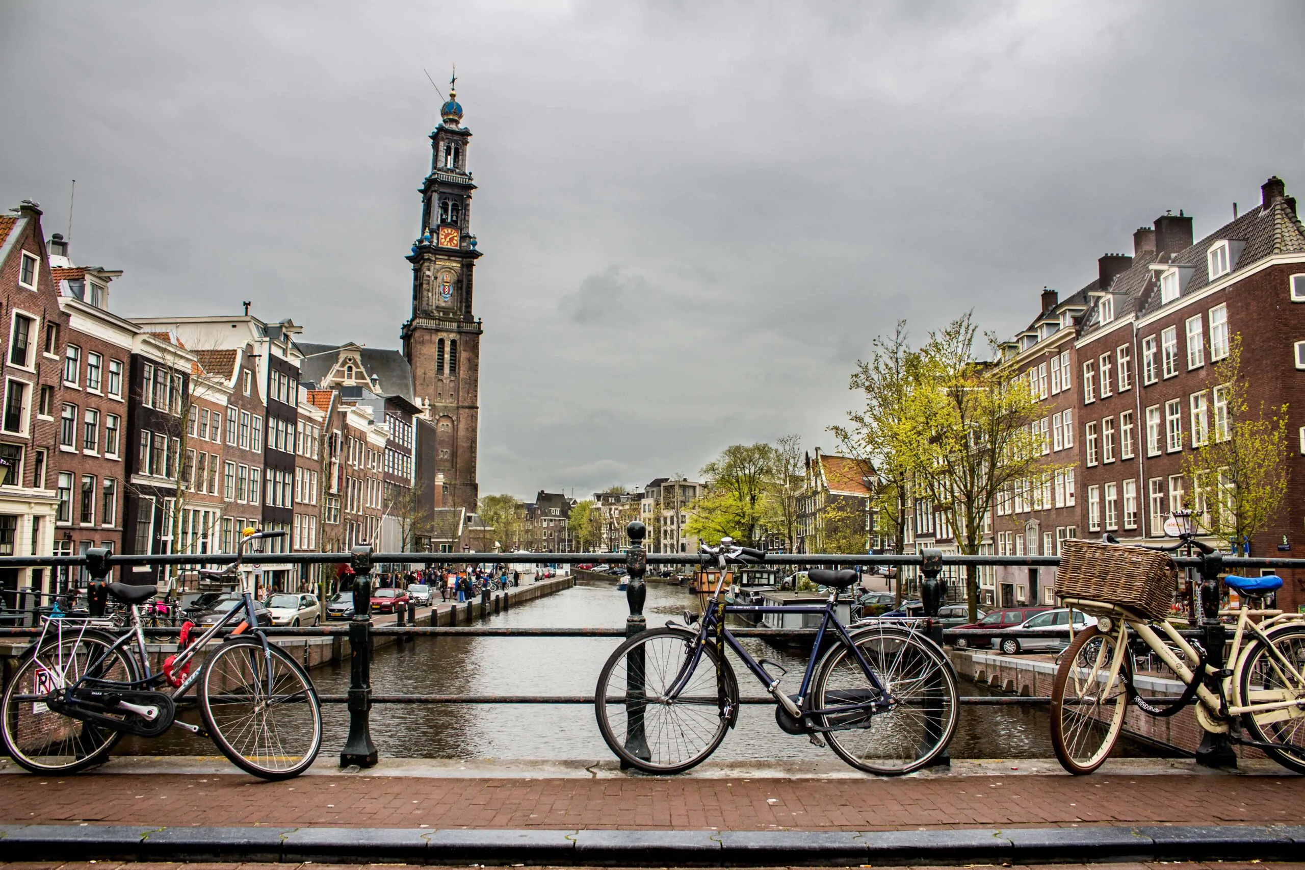 A beautiful shot of bicycles leaned again the fence on a bridge over the river in the middle of the building under a cloudy sky